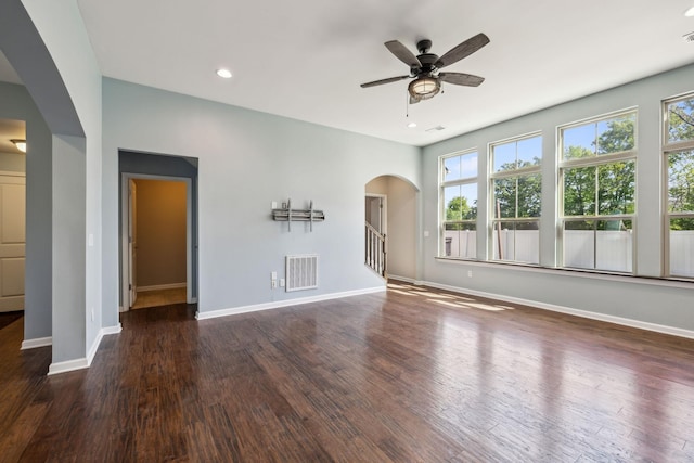 unfurnished living room featuring visible vents, wood finished floors, baseboards, ceiling fan, and arched walkways