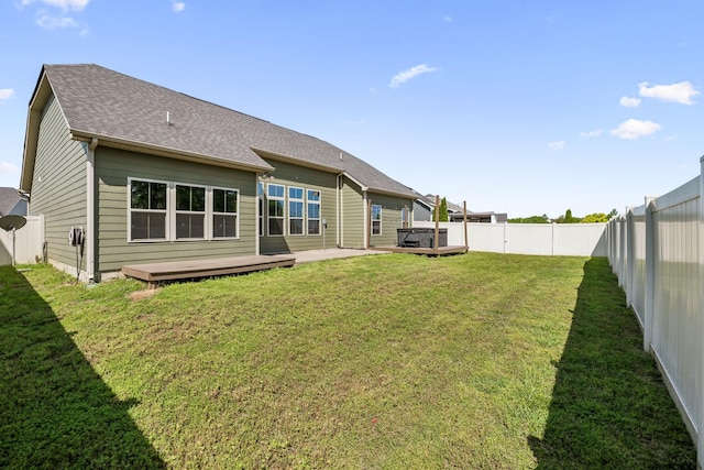 rear view of property with a lawn, a fenced backyard, a hot tub, and a shingled roof