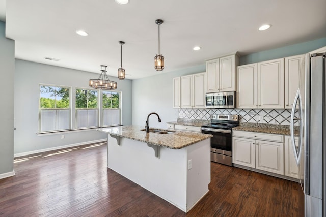 kitchen featuring a kitchen island with sink, light stone countertops, a sink, appliances with stainless steel finishes, and backsplash