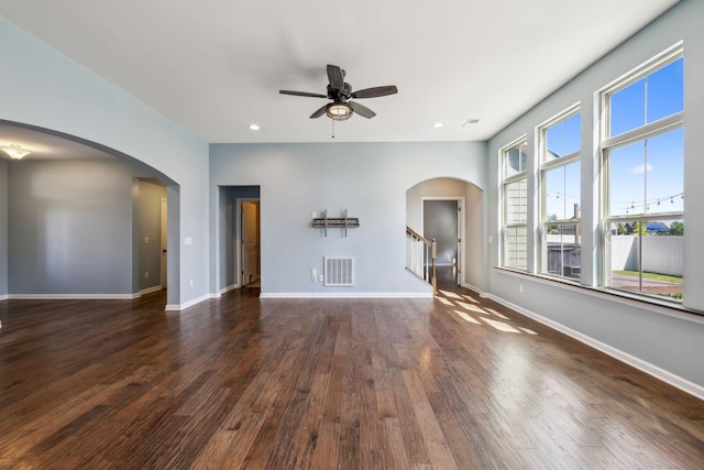 unfurnished living room with visible vents, arched walkways, dark wood finished floors, and ceiling fan