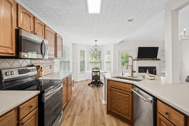 kitchen with brown cabinetry, light wood-type flooring, a textured ceiling, a sink, and stainless steel appliances