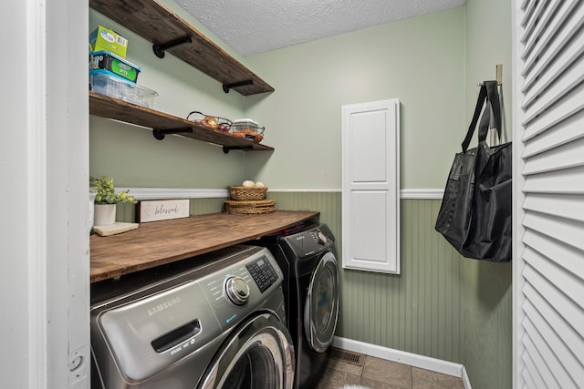 washroom featuring a textured ceiling, wainscoting, cabinet space, baseboards, and separate washer and dryer