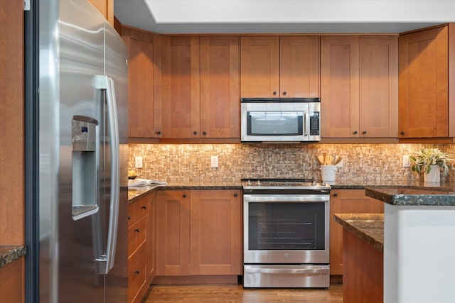 kitchen featuring brown cabinetry, dark stone counters, tasteful backsplash, and stainless steel appliances