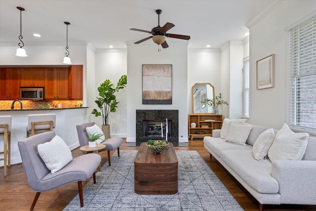 living room featuring a high end fireplace, a ceiling fan, wood finished floors, and ornamental molding