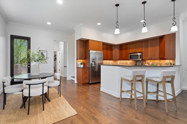 kitchen with brown cabinetry, stainless steel appliances, a peninsula, decorative backsplash, and dark wood-style floors