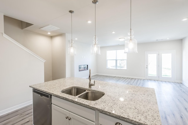 kitchen featuring light wood-style flooring, a center island with sink, dishwasher, a sink, and white cabinetry