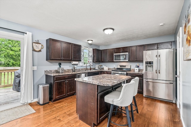 kitchen featuring appliances with stainless steel finishes, dark brown cabinetry, a breakfast bar, and light wood-type flooring