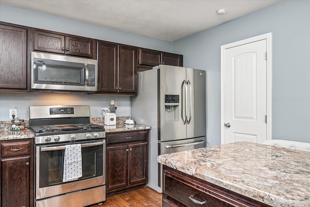 kitchen with light stone counters, dark brown cabinetry, stainless steel appliances, and dark wood-type flooring