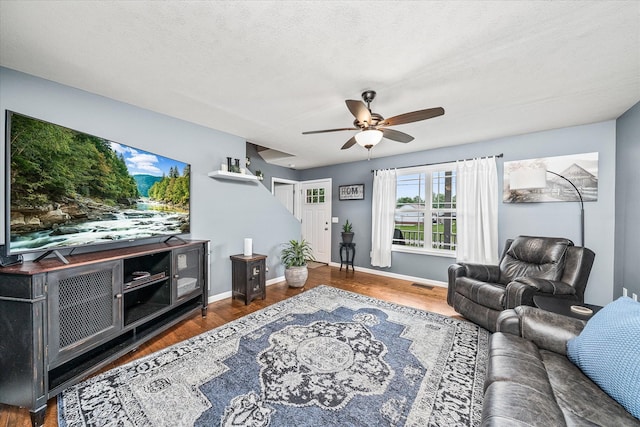 living area featuring ceiling fan, a textured ceiling, baseboards, wood finished floors, and visible vents
