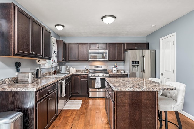kitchen featuring dark brown cabinetry, appliances with stainless steel finishes, a sink, a breakfast bar area, and wood finished floors