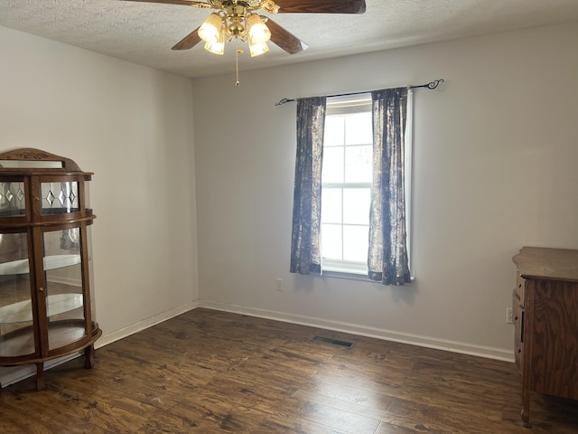 empty room with a ceiling fan, dark wood finished floors, a wealth of natural light, and visible vents