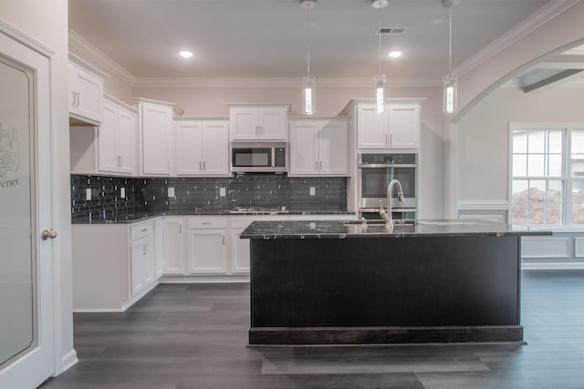kitchen featuring arched walkways, gas stovetop, stainless steel microwave, ornamental molding, and white cabinetry