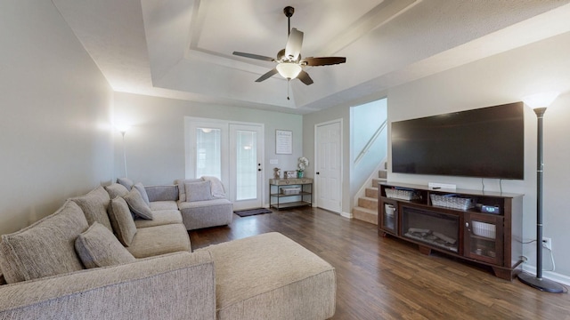 living room featuring stairs, dark wood-style flooring, a tray ceiling, and ceiling fan