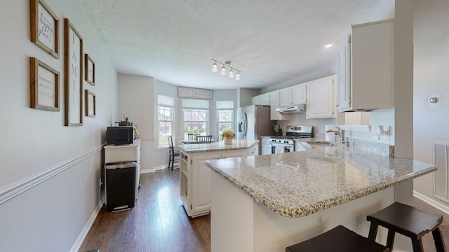 kitchen featuring appliances with stainless steel finishes, a sink, baseboards, under cabinet range hood, and a kitchen island