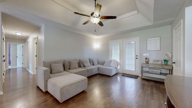 living room with dark wood-type flooring, attic access, ceiling fan, and a tray ceiling
