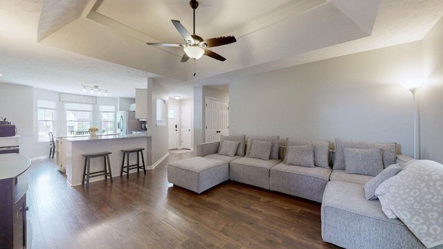 living room featuring baseboards, a raised ceiling, ceiling fan, and dark wood-style floors