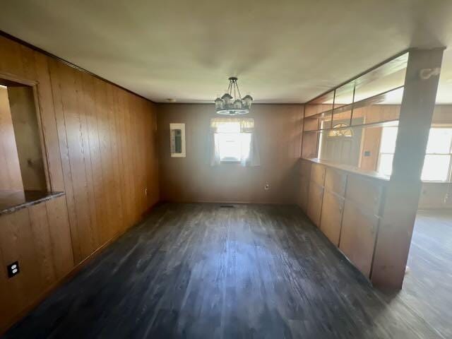 unfurnished dining area featuring an inviting chandelier, wood walls, wood finished floors, and a healthy amount of sunlight