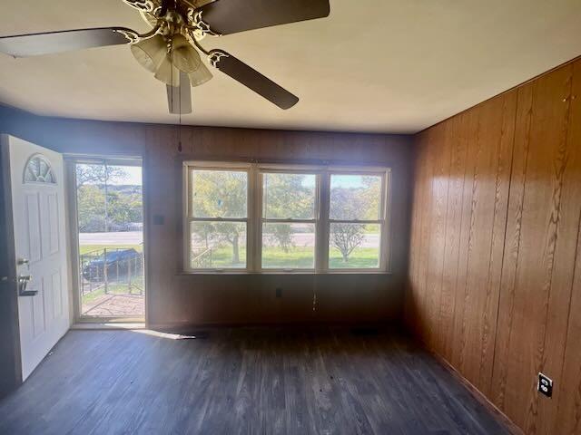 empty room with wooden walls, a ceiling fan, and wood finished floors