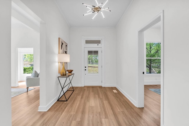 foyer with an inviting chandelier, ornamental molding, light wood finished floors, and a wealth of natural light