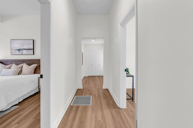 hallway with baseboards, visible vents, and light wood-type flooring