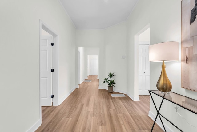 corridor featuring baseboards, ornamental molding, and light wood-style flooring