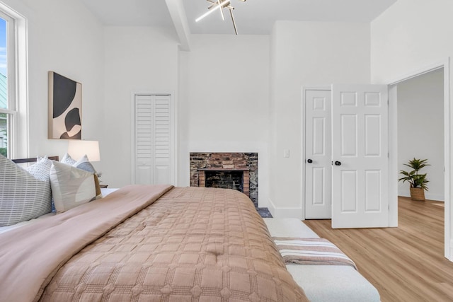 bedroom with baseboards, a fireplace, light wood-style flooring, and a towering ceiling