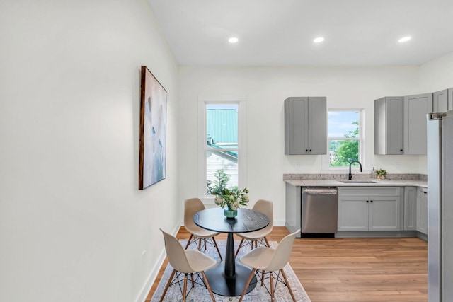 kitchen with gray cabinetry, light countertops, a sink, stainless steel appliances, and light wood-style flooring