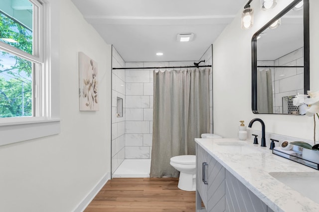 bathroom featuring double vanity, a tile shower, wood finished floors, a sink, and toilet