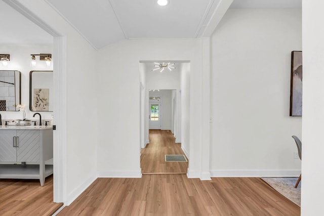 hallway featuring visible vents, light wood-style flooring, lofted ceiling, and baseboards