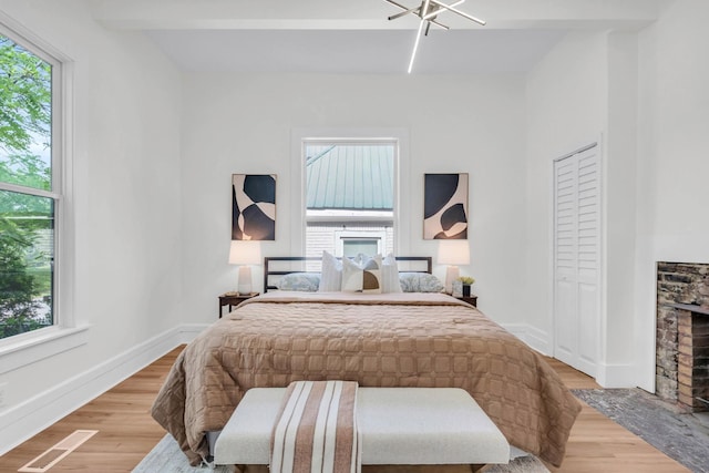 bedroom with light wood-style floors, a fireplace with flush hearth, and visible vents