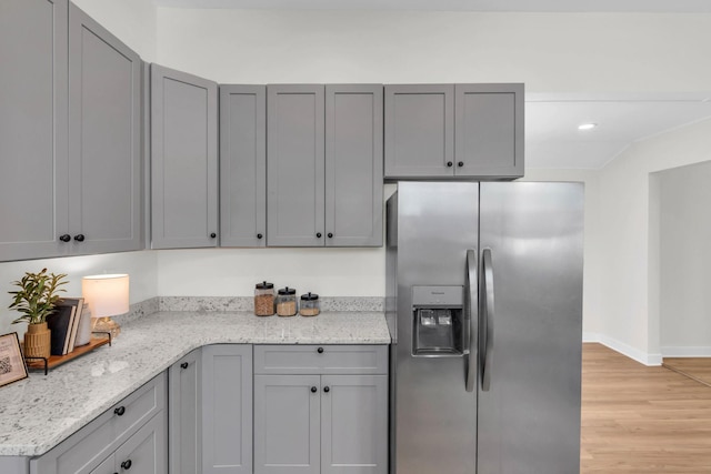kitchen featuring stainless steel fridge, light stone counters, gray cabinetry, and light wood finished floors