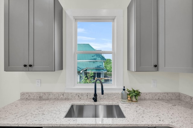 kitchen featuring light stone countertops, gray cabinetry, and a sink