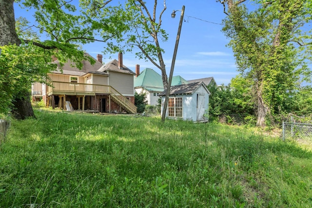 view of yard featuring fence, a deck, stairs, a storage unit, and an outbuilding