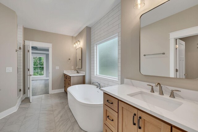 bathroom with a soaking tub, baseboards, two vanities, and a sink