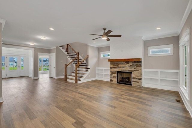 unfurnished living room with stairs, a ceiling fan, a stone fireplace, and wood finished floors