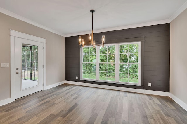 unfurnished dining area with baseboards, a chandelier, ornamental molding, and wood finished floors