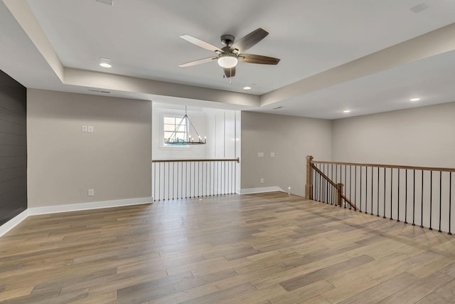 spare room with baseboards, wood finished floors, and ceiling fan with notable chandelier
