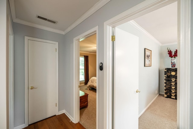 hall with baseboards, visible vents, ornamental molding, and dark carpet