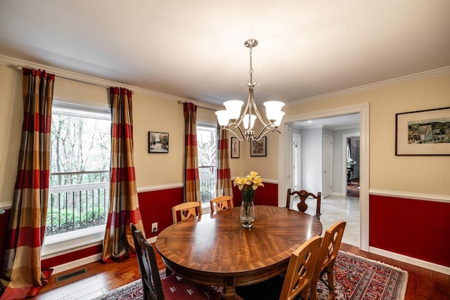 dining room featuring a notable chandelier, wood-type flooring, baseboards, visible vents, and ornamental molding