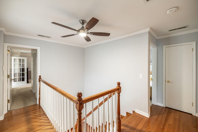 corridor featuring visible vents, ornamental molding, wood finished floors, and an upstairs landing