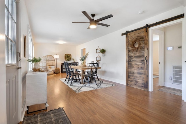 dining area featuring ceiling fan, visible vents, a barn door, wood finished floors, and baseboards
