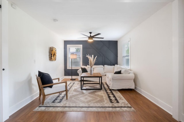 living area with a healthy amount of sunlight, baseboards, an accent wall, and ceiling fan