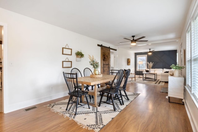 dining area with a ceiling fan, visible vents, a barn door, wood finished floors, and baseboards