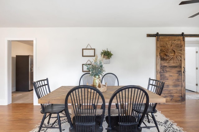 dining area with a barn door, a ceiling fan, and wood finished floors
