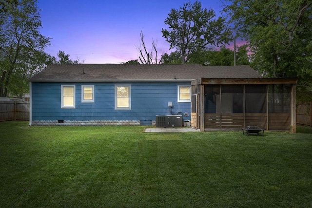 back of property at dusk featuring fence, a lawn, and a sunroom