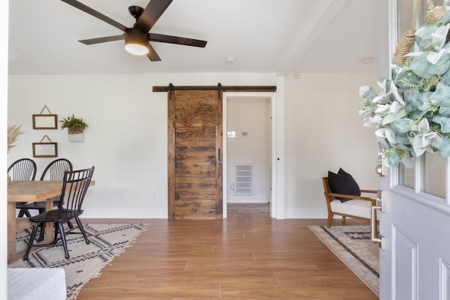interior space featuring a ceiling fan, visible vents, light wood-type flooring, a barn door, and baseboards