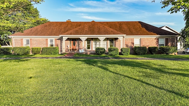 ranch-style home featuring a shingled roof, a chimney, brick siding, and a front yard