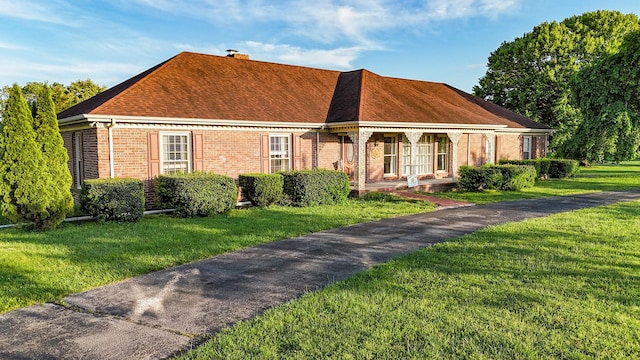 view of front facade with brick siding, a front lawn, a chimney, and a porch