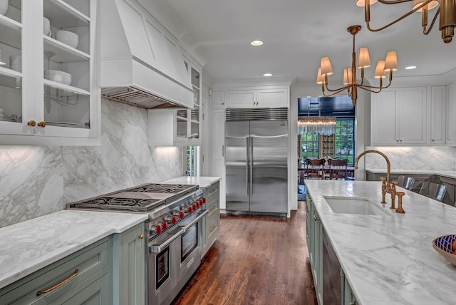 kitchen with a sink, light stone counters, custom exhaust hood, a chandelier, and premium appliances