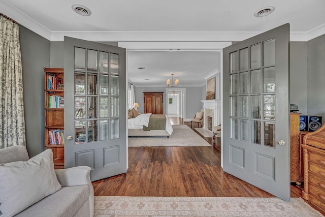 interior space featuring crown molding, wood finished floors, visible vents, and an inviting chandelier